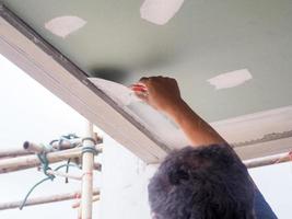 o trabalhador do teto está rebocando as juntas do teto com gesso branco de alta qualidade para manter as juntas juntas. foto