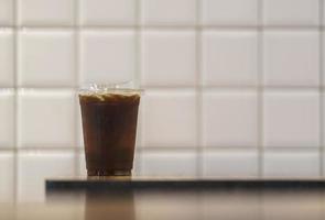 closeup de copo de plástico para viagem de café preto gelado americano na mesa de madeira no restaurante. foto