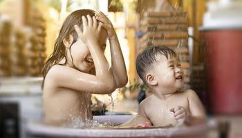 a irmã e o irmão mais velhos estavam alegremente tomando banho de banheira de plástico pela manhã. tomar um banho ao ar livre em um dia quente. irmãos estão felizes em brincar na água. crianças se divertindo brincando na água foto