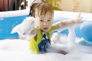 menino bonitinho se divertindo brincando com bolhas em uma piscina inflável nas férias de verão. brincando na água em casa durante as férias de verão, a felicidade das crianças foto