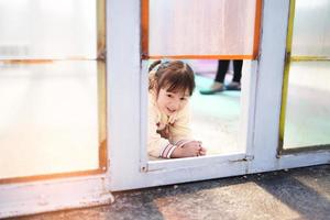 menina jogando alegremente olha pela janela de vidro colorido. foto