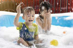 menino bonitinho e irmã se divertem brincando com bolhas e bolas coloridas na piscina inflável. piscinas infláveis e de bolhas, nadar no verão, crianças felizes brincando na água foto