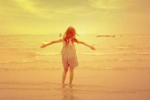 criança feliz se divertindo a pé na praia ao pôr do sol. adorável menina brincando ao longo da água do mar. conceito de dias de verão de infância e liberdade foto