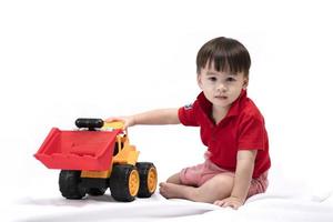 menino bonitinho sentado e jogando escavadeira de brinquedo em fundo branco. crianças felizes brincando de brinquedos foto