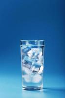 um copo com água gelada e cubos de gelo em um fundo azul. foto