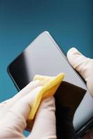 desinfecção do smartphone com um guardanapo amarelo com impregnação antibacteriana em luvas de mão. foto