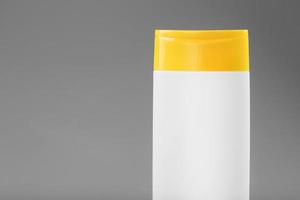 garrafa de plástico branca com tampa amarela com gel de xampu em fundo cinza foto
