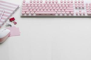 teclado de computador rosa com mouse e suprimentos em uma mesa branca foto