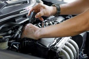 feche a bobina da vela de ignição na mão, um homem remove do serviço do motor a gasolina na garagem e no fundo da sala de máquinas foto