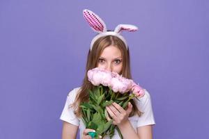 mulher jovem e bonita com orelhas de coelhinho da páscoa rosa em fundo roxo em branco foto