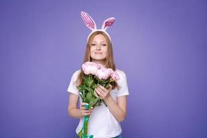 encantadora linda garota feliz com orelhas de coelhinho da páscoa rosa e primavera de buquê foto
