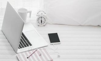 laptop com relógio, telefone e café na cama foto