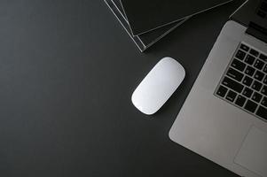 laptop, mouse e livros em uma mesa preta foto