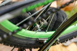 homem mecânico de bicicleta repara bicicleta na oficina de bicicletas, ao ar livre. mão de ciclista examina, corrige o sistema de transmissão de ciclo moderno. manutenção de bicicletas, conceito de loja de esportes. foto