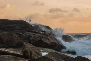 pescador nas rochas durante o pôr do sol foto