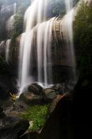 cachoeira tad wimanthip com belas rochas e turistas em capas de chuva estão admirando a beleza da cachoeira.