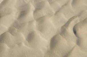 fundo de textura de areia do deserto ondulado. areia fina amarela da praia. fundo de textura de areia dourada, conceito de férias de sol de verão. a textura da areia da praia como pano de fundo. foto
