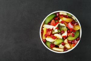 salada de frutas em um copo branco em um fundo preto, espaço livre para texto. foto