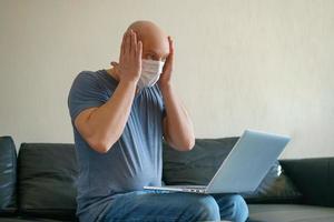 um homem adulto careca se comunica em um laptop em casa no sofá, mostra um gesto com a mão. o conceito de comunicação na quarentena foto