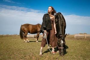 mulher jovem e bonita em um campo com cavalos. modelo de moda atraente. foto