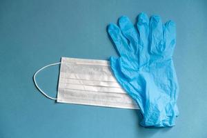 máscara branca cirúrgica e luvas de látex para proteção em um fundo azul foto