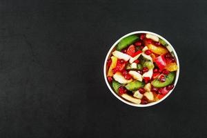 salada de frutas em um copo branco em um fundo preto, espaço livre para texto. foto