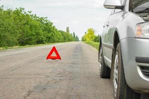 sinal vermelho de parada de emergência e carro prateado quebrado na estrada foto