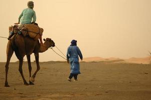 um homem montado em um camelo sendo conduzido pelo deserto foto