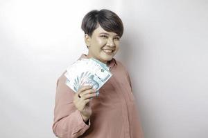 uma jovem feliz está vestindo camisa rosa e segurando dinheiro em rupia indonésia isolada por fundo branco foto