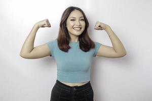 mulher asiática animada vestindo uma camiseta azul mostrando um gesto forte, levantando os braços e os músculos sorrindo orgulhosamente foto