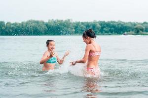 duas adolescentes estão espirrando uma na outra no rio. turismo local. férias de verão foto