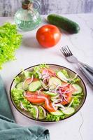 tomate, pepino, cebola, salada de alface em um prato na mesa. comida vegetariana. visão vertical foto