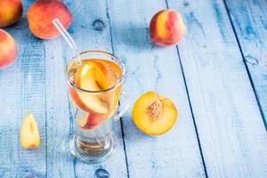 compota de pêssegos frescos em um copo com um canudo na mesa. bebidas orgânicas de verão foto