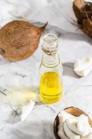 óleo de coco vegetal fresco em uma garrafa e pedaços de coco em cima da mesa. vista vertical e acima foto