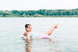 uma garota alegre nada em um anel inflável no rio e estica as pernas. turismo local. férias de verão foto