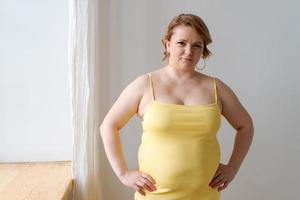 retrato alegre atraente jovem gorda plus size mulher em vestido amarelo apertado foto