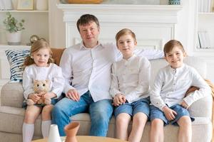 pai feliz com três crianças sentadas no sofá olhando uns aos outros foto
