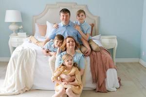 feliz família grande caucasiana com filhos bonitos sentados no quarto ao lado da cama, as crianças riem foto