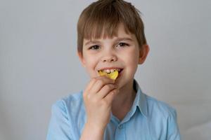 jovem criança caucasiana comendo batatas fritas insalubres em um fundo cinza foto