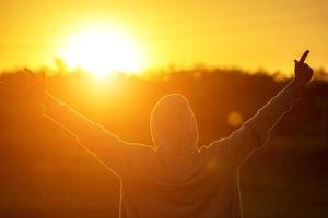 um homem à luz do pôr do sol com as mãos para cima, o conceito de sucesso, liberdade e alegria foto