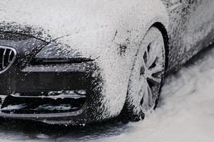 carro preto moderno coberto por espuma. lave água de alta pressão e sabão. close-up de auto na estação de lavagem de carros. serviço de limpeza de veículos foto