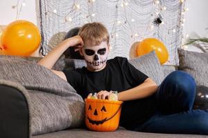 um menino com maquiagem de esqueleto tira doces de uma festa de halloween. foto