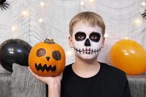 criança assustadora com uma maquiagem em forma de esqueleto e com uma abóbora nas mãos foto