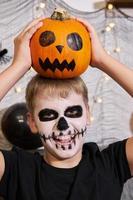 adolescente com maquiagem no rosto e com uma abóbora nas mãos para o halloween. foto