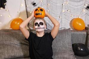 adolescente com maquiagem no rosto e com uma abóbora nas mãos para o halloween. foto