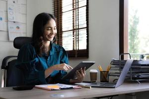 jovem empresária asiática trabalha em tablet com laptop no escritório. foto