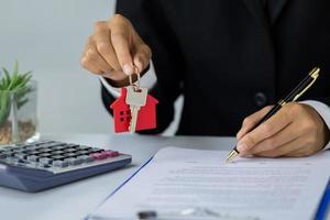 uma mulher assina um contrato para comprar uma casa com um agente imobiliário. modelo de casa e chaves nas mãos de empresários. foto