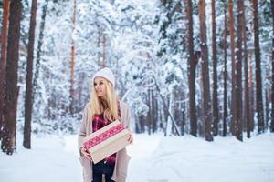 garota segurando um presente de natal na floresta de inverno