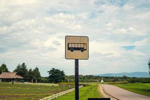 ponto de ônibus à moda antiga perto da estrada de asfalto cercada por grama verde, montanhas e fazenda. conceito de viagem por estrada de cena de natureza rural e espaço de cópia para propaganda. foto