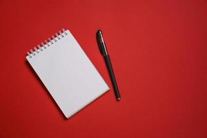 caderno aberto em uma mola e uma caneta esferográfica preta em uma cópia de fundo vermelho foto